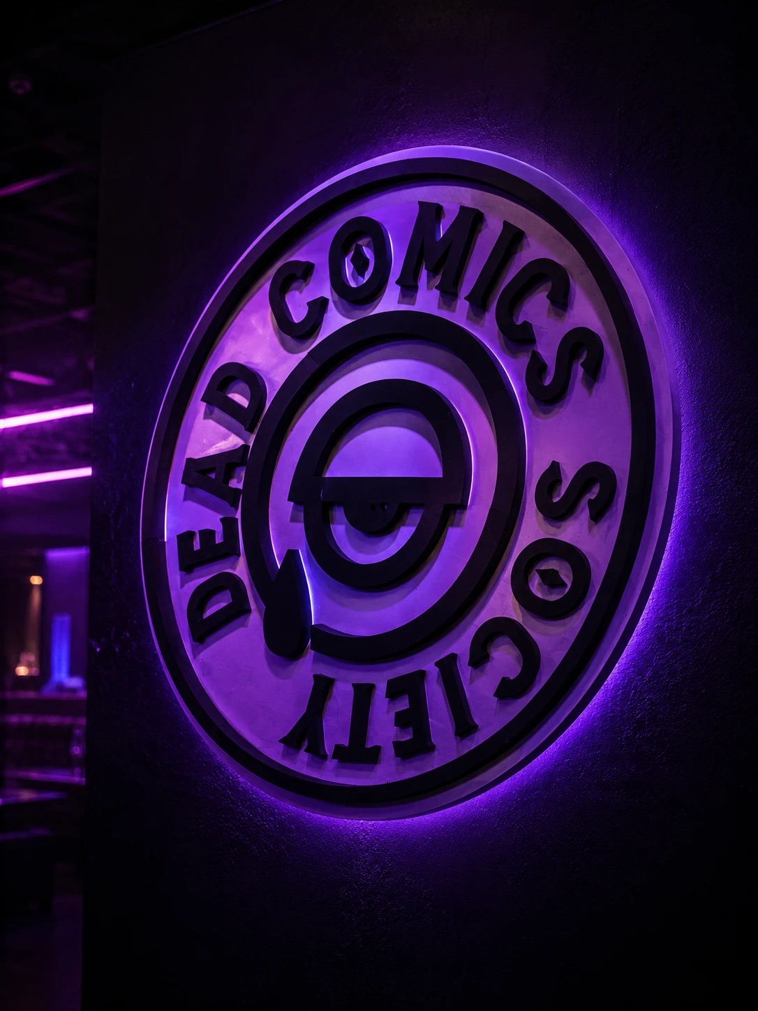 The Dead Comics Society sign backlit in purple on the venue wall